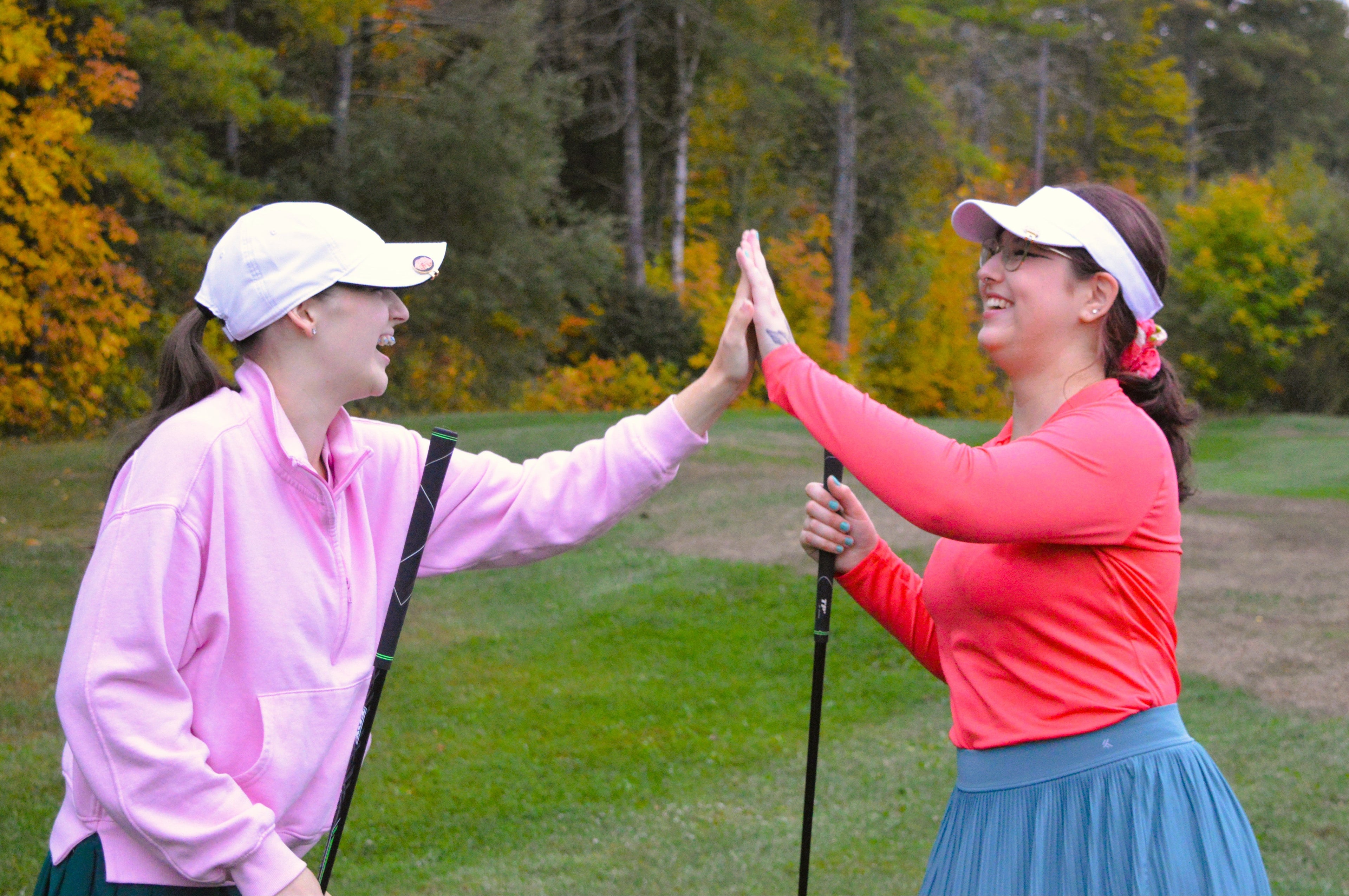 Two women on a golf course giving each other a high-five with trees in the background.